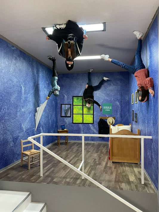 People are upside down in a room with blue walls and a bed, creating an optical illusion.