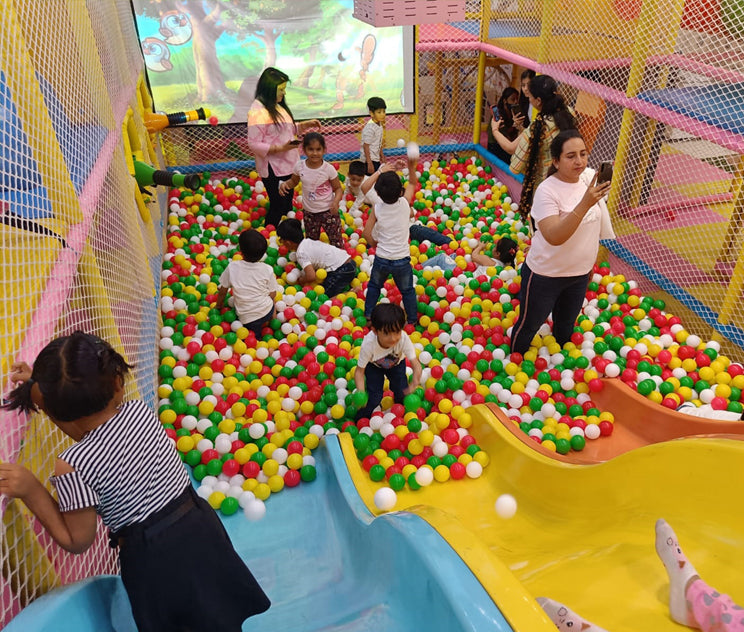 Children playing in a colorful ball pit with adults supervising in an indoor playground.