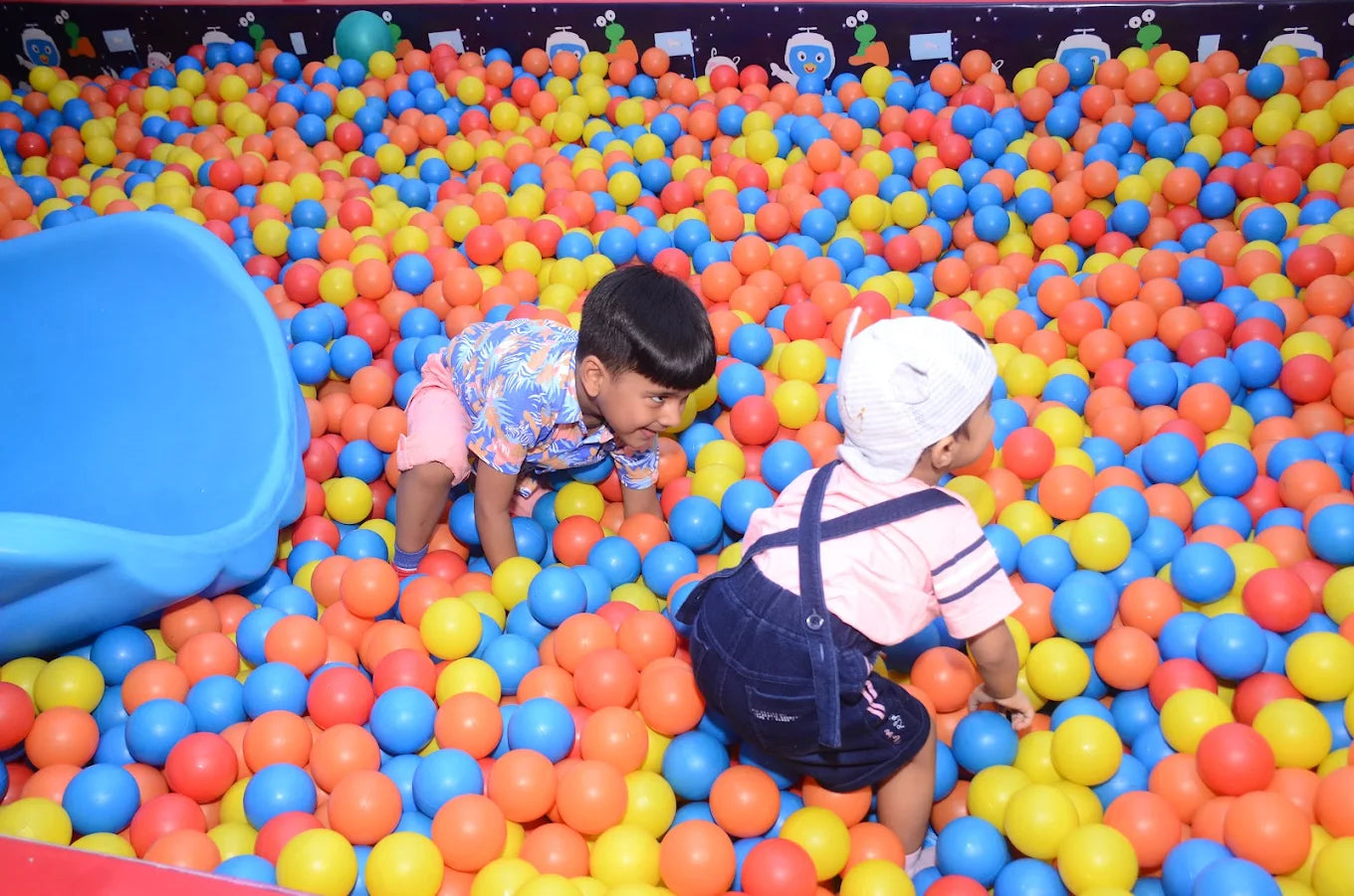Two children playing in a colorful ball pit at an indoor playground.