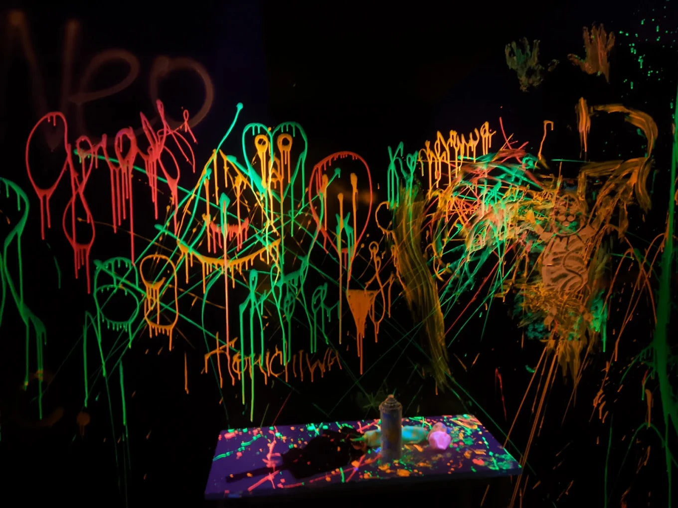 Neon graffiti art covers a dark wall, with a table of spray paint cans in the foreground.