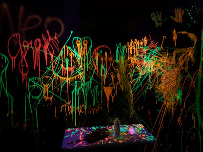 Neon graffiti art covers a dark wall, with a table of spray paint cans in the foreground.