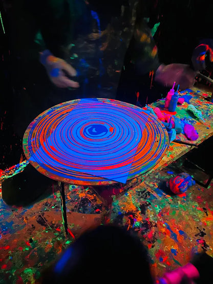 People create a swirling paint pattern on a spinning canvas under blacklight.