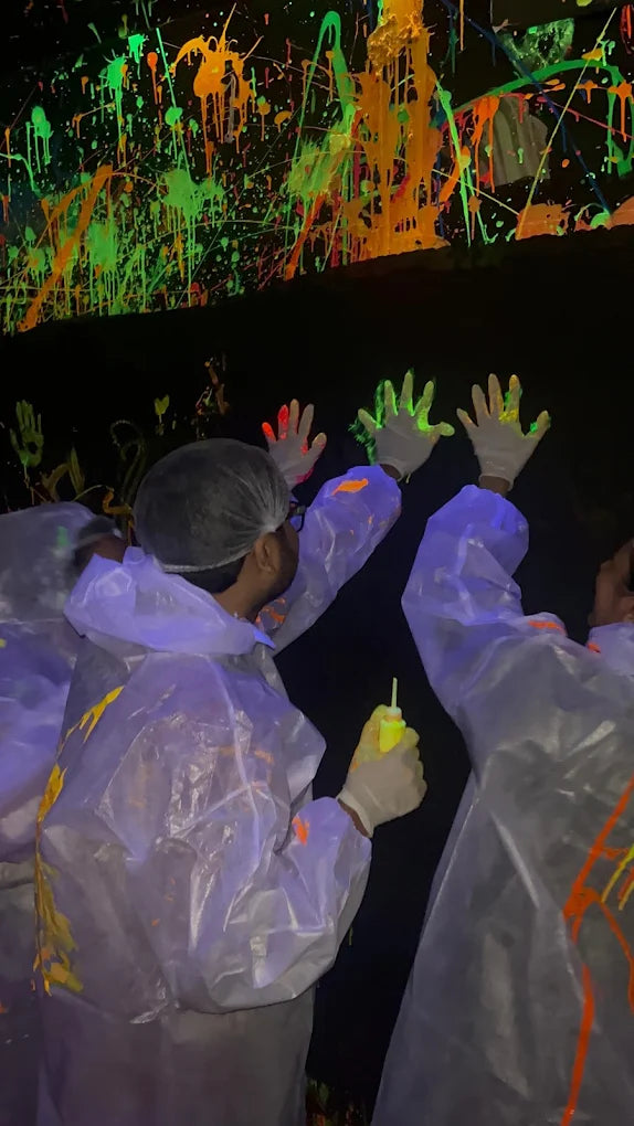 People in protective suits make handprints with glowing paint on a black wall.