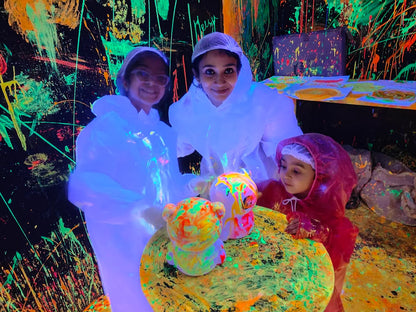 Three people in protective suits paint colorful figures in a neon-lit room.