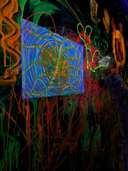 A person paints a neon spiderweb on a black wall covered in dripping paint.