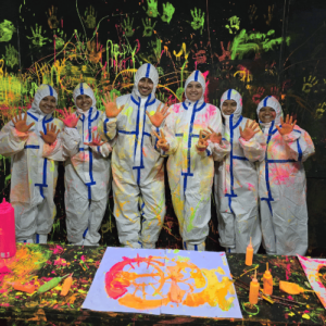 Young people in protective suits create colorful art with neon paint under blacklight.