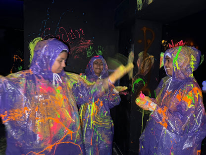 Young people in colorful ponchos play with neon paint in a dark room.