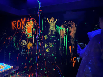 Children paint with neon colors on a black wall under blacklights.