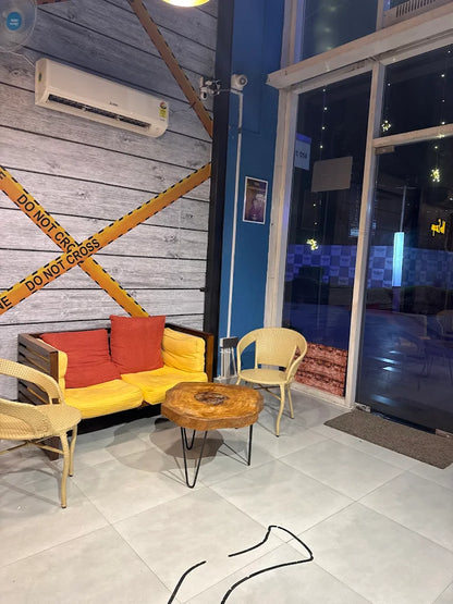 A modern seating area with a yellow couch, chairs, and a wooden table. The wall has "DO NOT CROSS" tape.