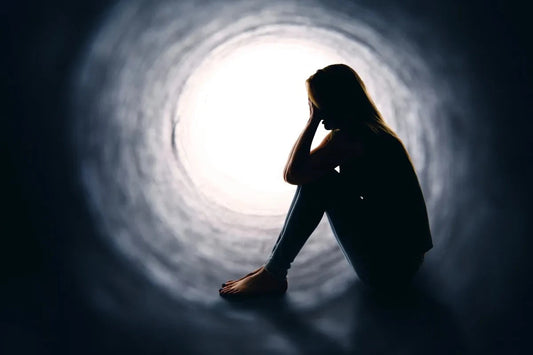 Silhouette of a young person sitting in a dark tunnel, facing a bright light.