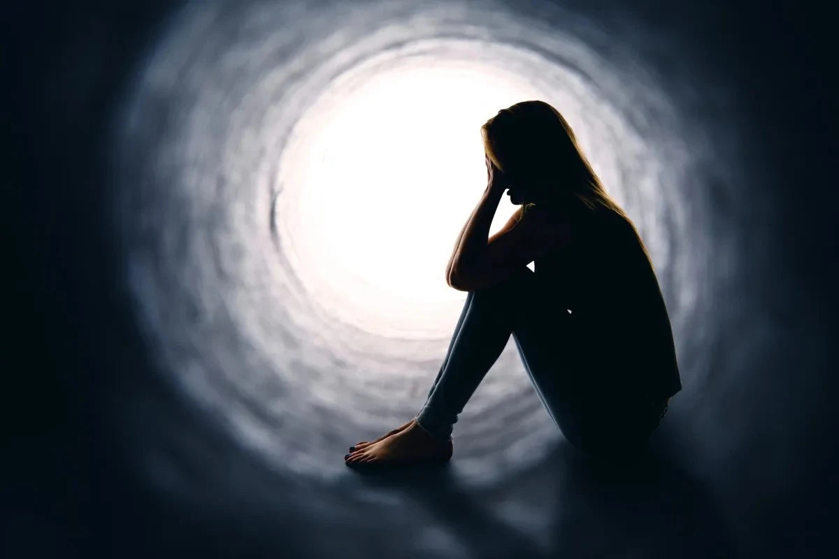 Silhouette of a young person sitting in a dark tunnel, facing a bright light.