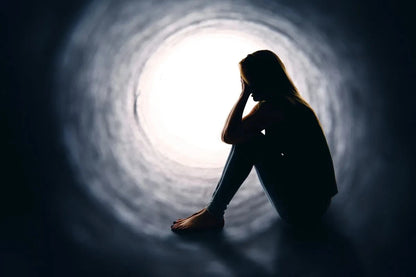 Silhouette of a young person sitting in a dark tunnel, facing a bright light.