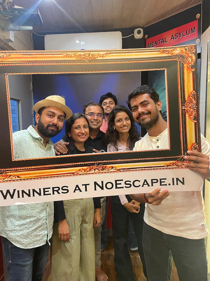 A group of young adults poses for a photo in a large ornate frame, holding a sign that reads "WINNERS AT NOESCAPE.IN".