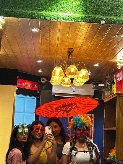 Four young women in a photo booth with props, including a colorful wig and novelty glasses.