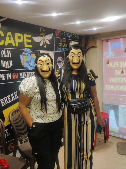 Two young women in Salvador Dalí masks pose in front of an escape room's themed wall.