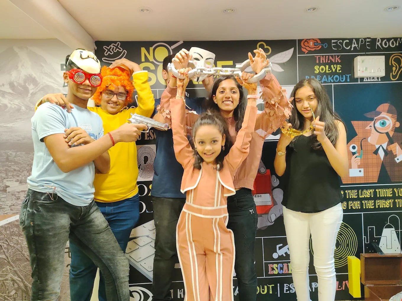 A group of young people in an escape room, posing with props like a chain and toy guns.