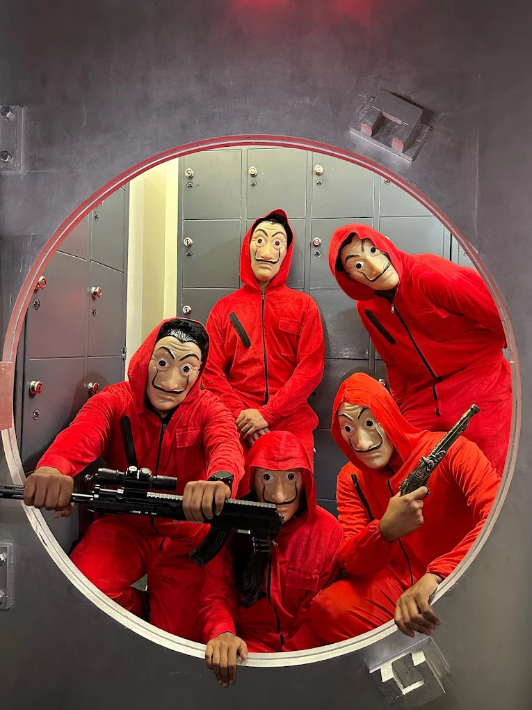 Five young people in red jumpsuits and Salvador Dalí masks pose with toy guns inside a vault.