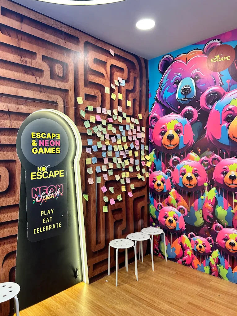 A brightly colored room with a maze mural, neon signs, and playful bear graphics, featuring white stools for guests.