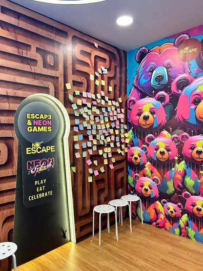 A brightly colored room with a maze mural, neon signs, and playful bear graphics, featuring white stools for guests.