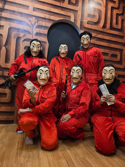 A group of young adults in red jumpsuits and Salvador Dalí masks pose in front of a maze-like backdrop.