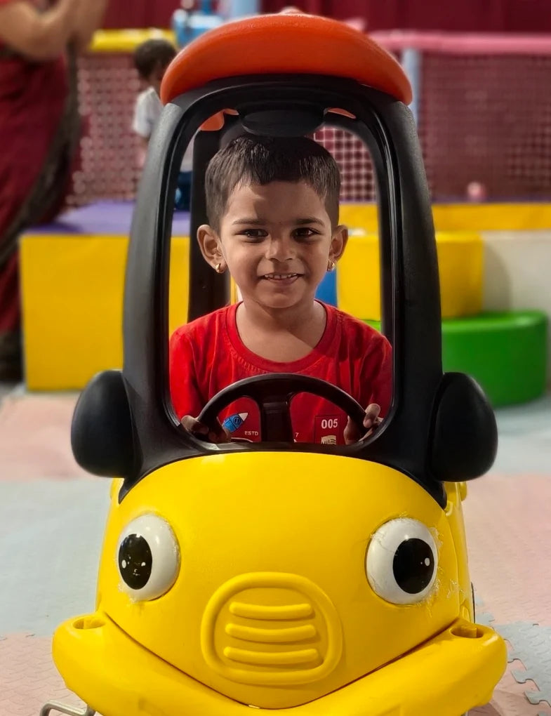 A young child smiles while sitting in a yellow toy car.