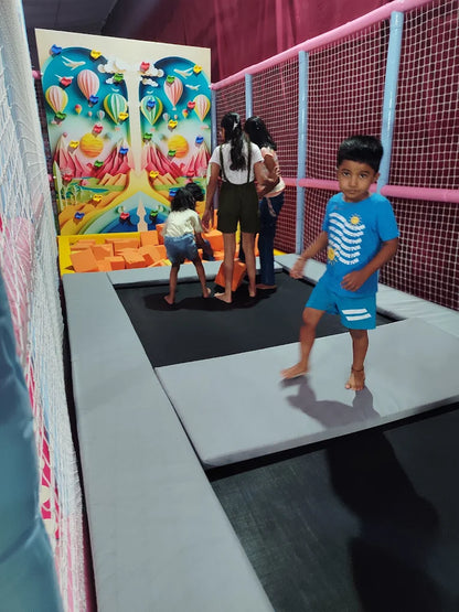 Children play on a trampoline in an indoor play area with a colorful mural.