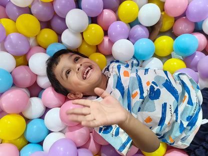 A young child smiles while lying in a ball pit filled with colorful balls.