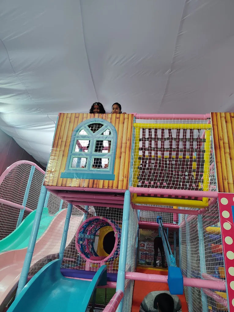 Two young girls peek over the railing of a colorful indoor playground structure.