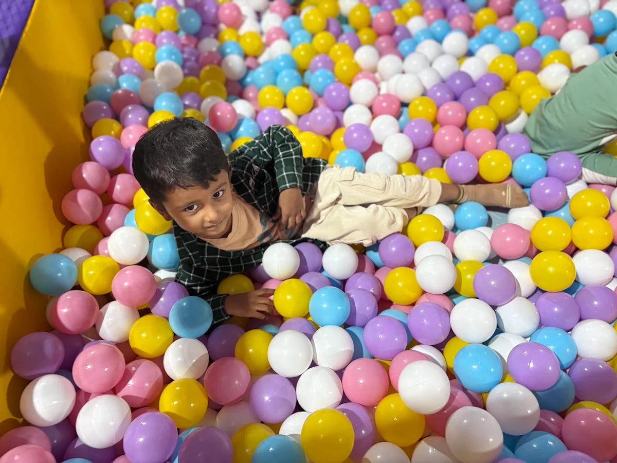 A young child lies in a ball pit filled with colorful balls.