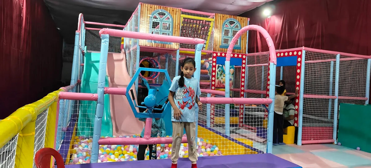 A young girl stands in a colorful indoor playground with ball pit.