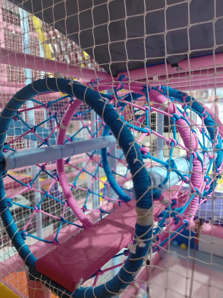 A colorful, netted play structure with blue and pink ropes and a pink mat.