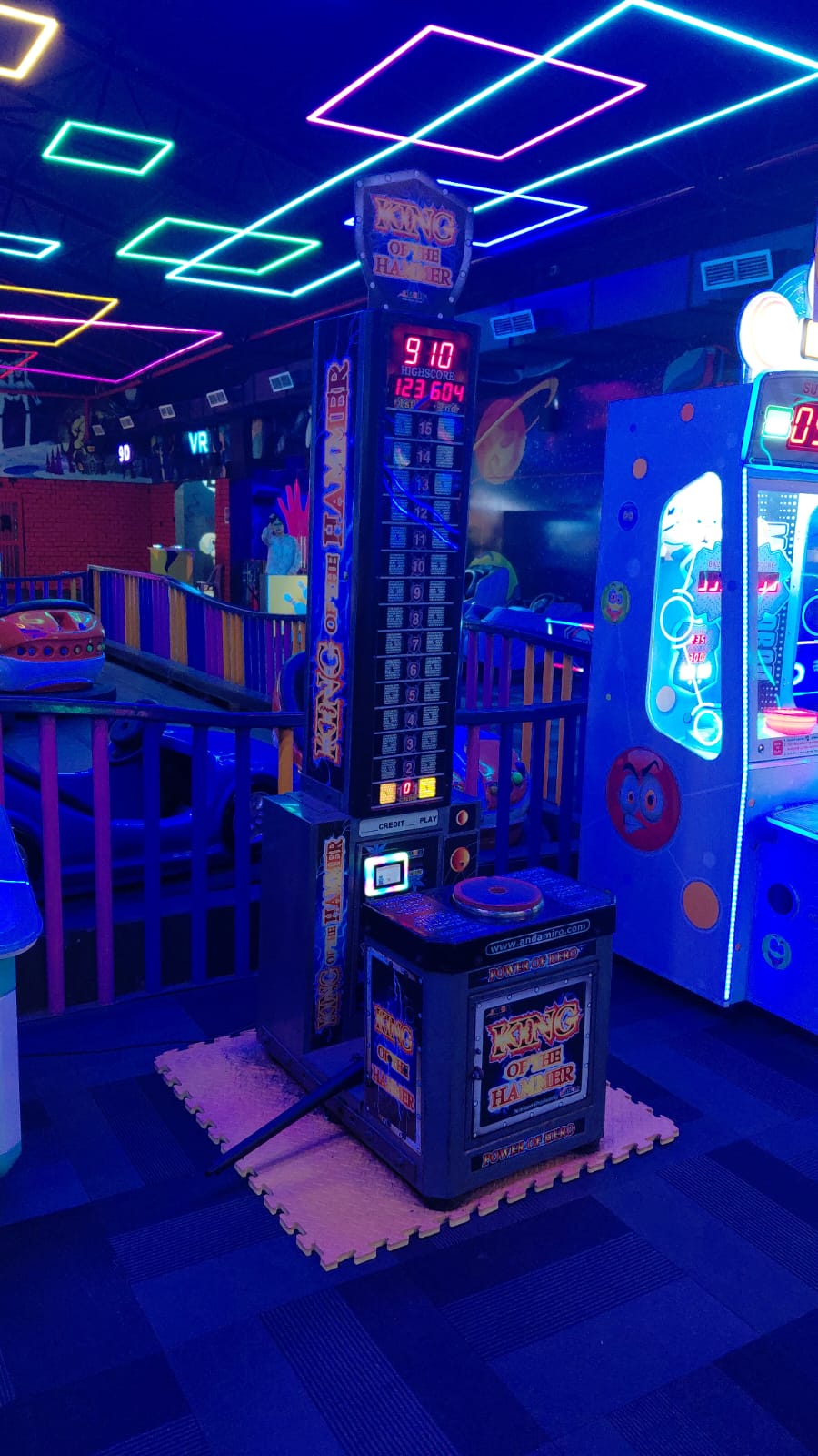 An arcade game called "King of the Hammer" is lit by neon lights in a dimly lit arcade.