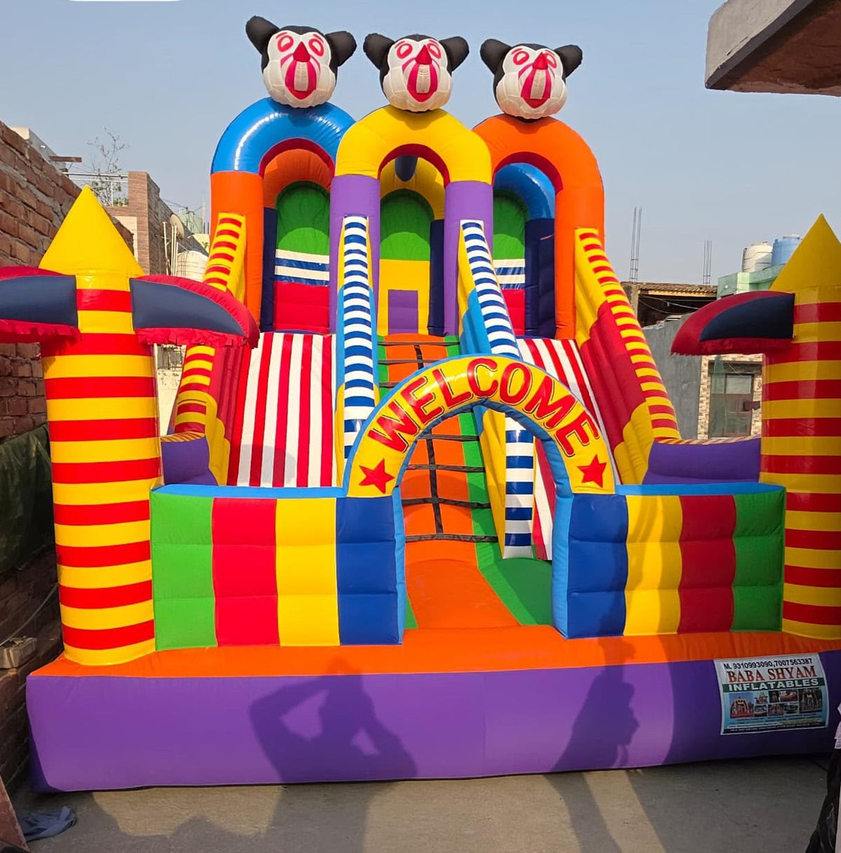 A colorful inflatable bounce house with Mickey Mouse characters and a "Welcome" arch, set outdoors.