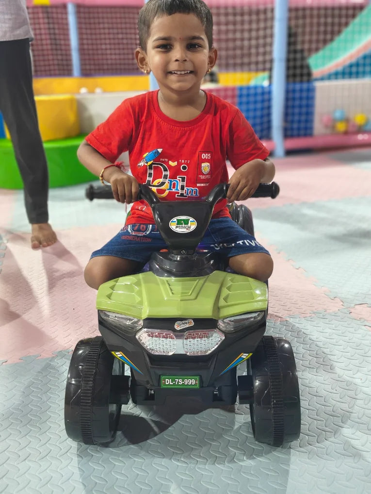 A young boy smiles while riding a toy ATV in an indoor play area.