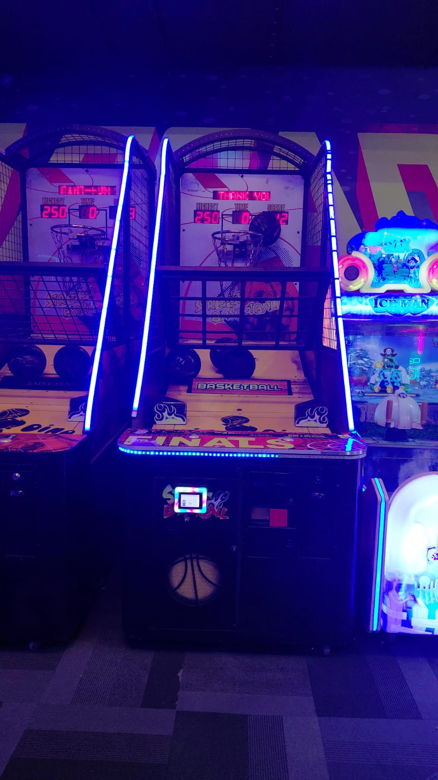 Two arcade basketball games are lit up with blue neon lights.