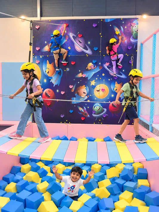 Children climb a space-themed wall while another child plays in a ball pit below.