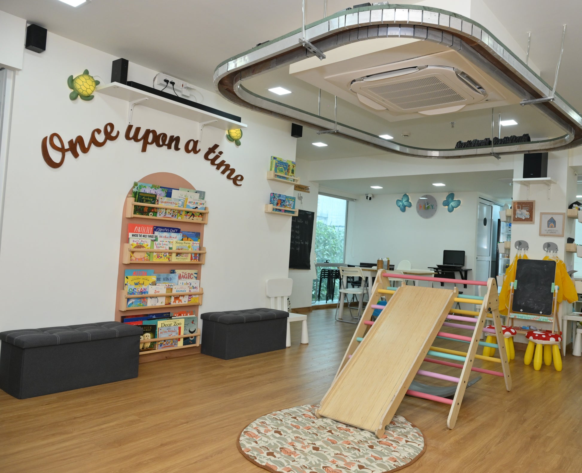 A bright, modern playroom with a wooden slide, bookshelves, and seating for young children.