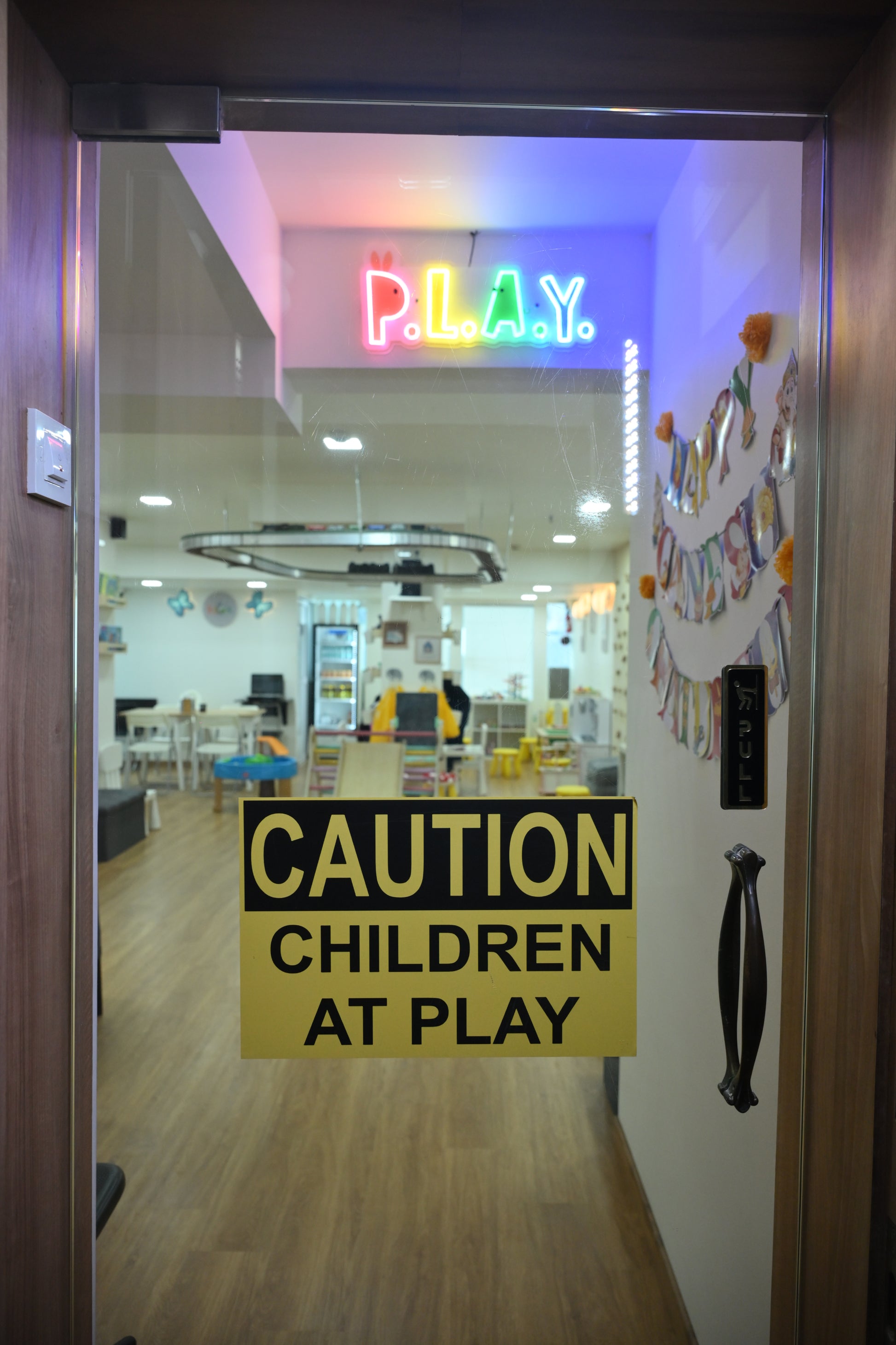 A glass door with a "Caution Children at Play" sign and neon "PLAY" sign.