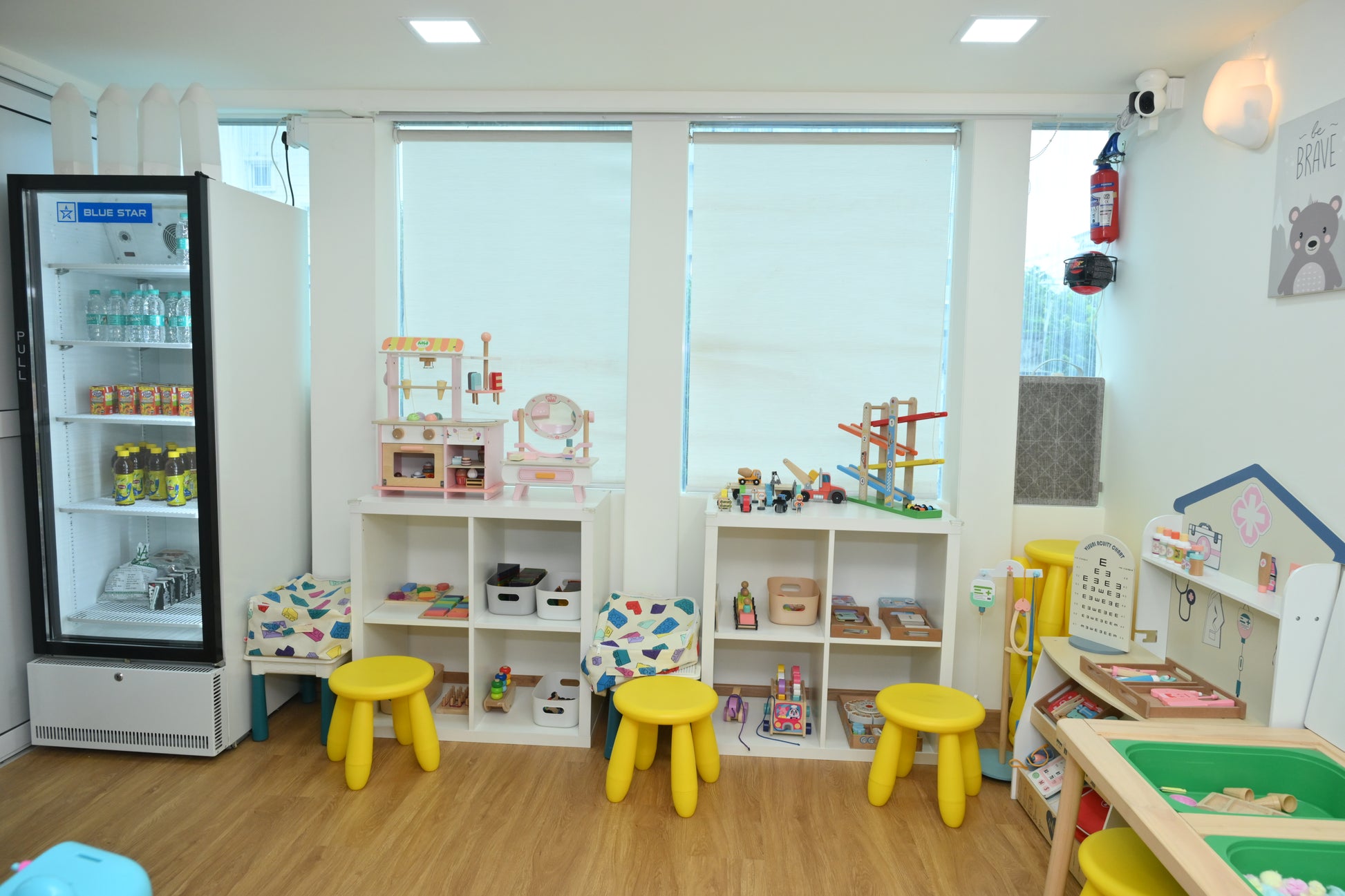 A brightly lit playroom with toys, a refrigerator, and children's furniture.
