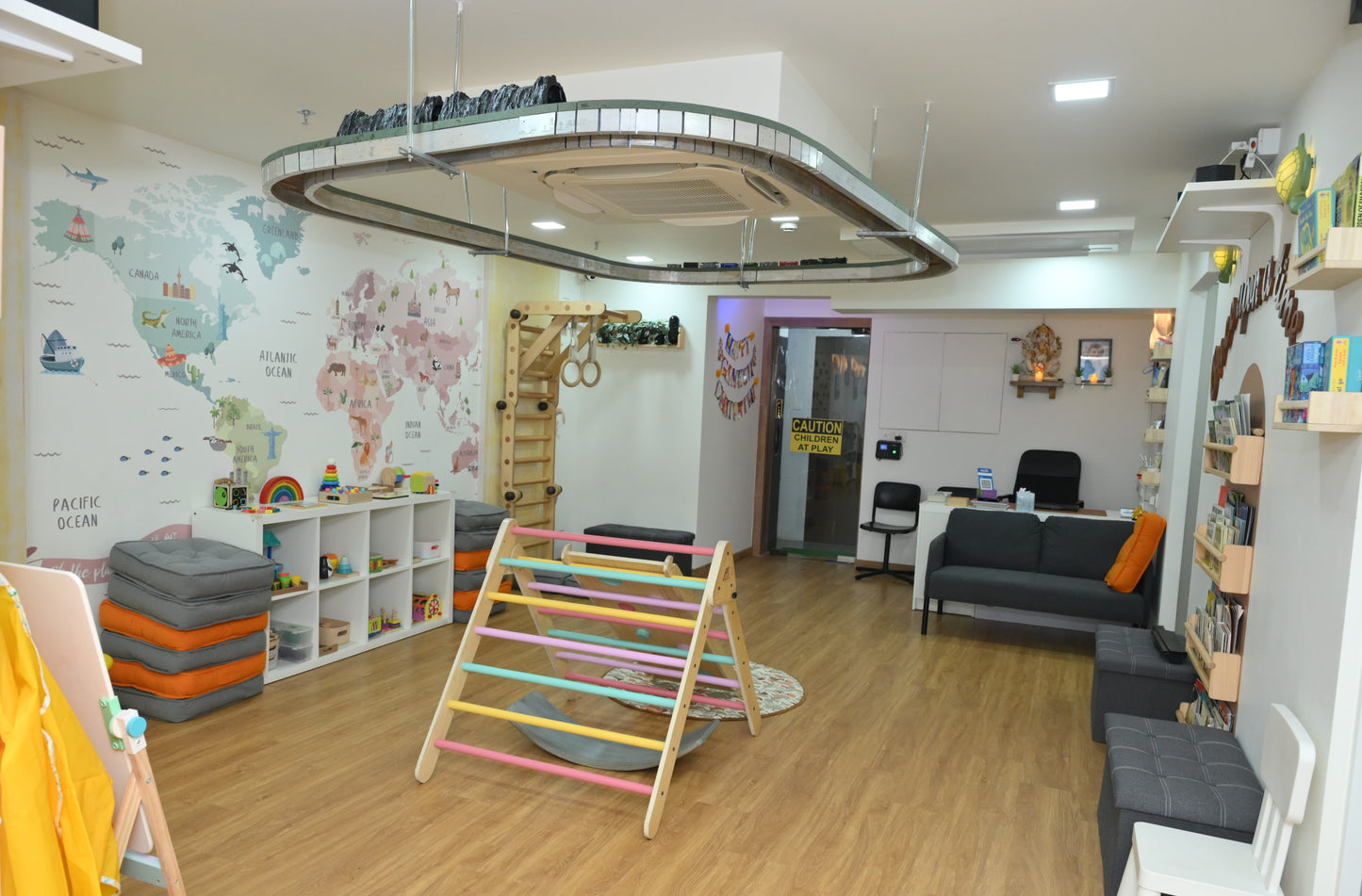 A brightly decorated children's playroom with a world map mural, climbing toys, and shelves of books.
