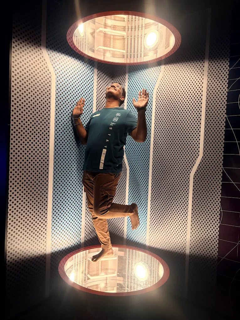 A man stands on one leg in a futuristic room with a light above and below.