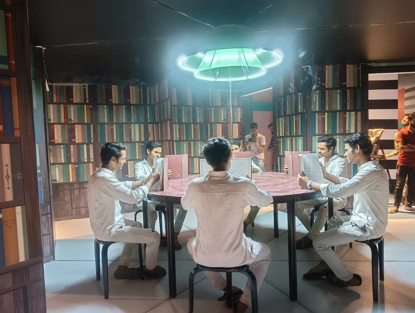 Young men in a library setting, reading books around a table.