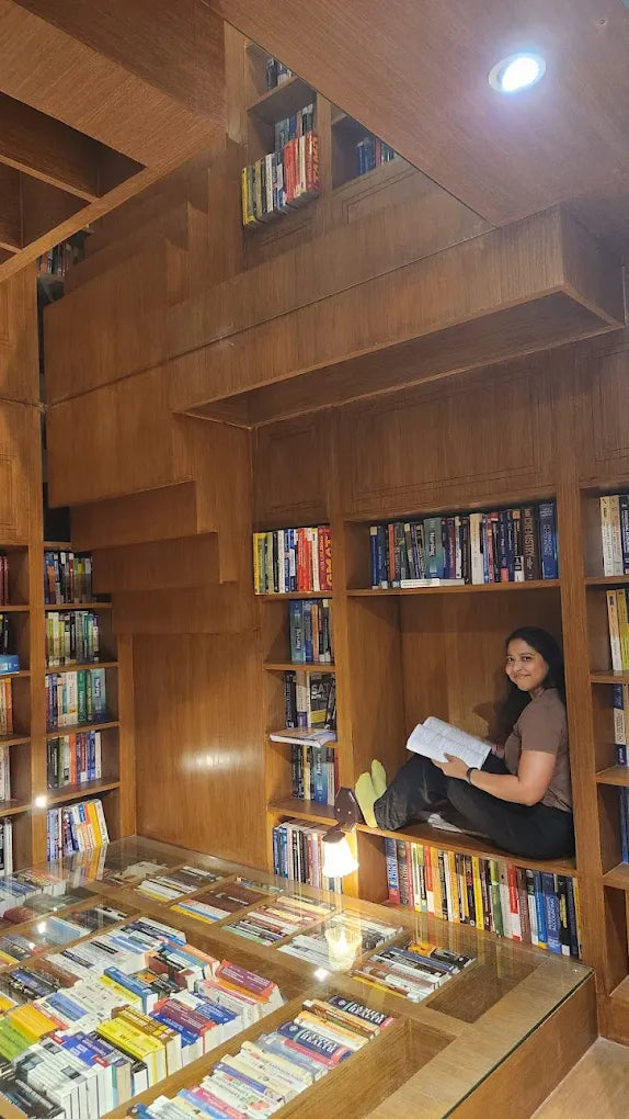 A young woman reads a book in a cozy nook surrounded by floor-to-ceiling bookshelves.