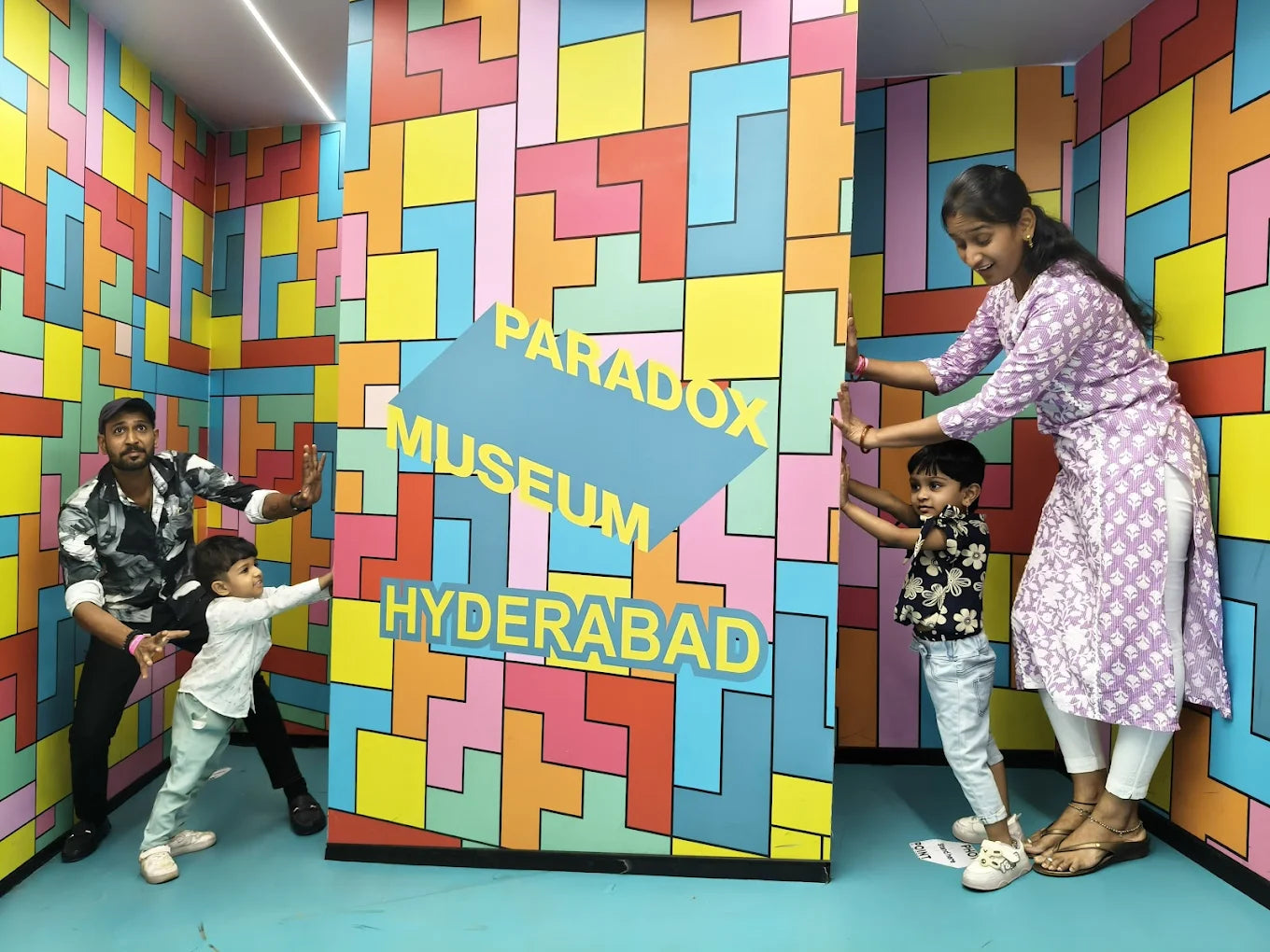 A family poses in a colorful room with a "Paradox Museum Hyderabad" sign.