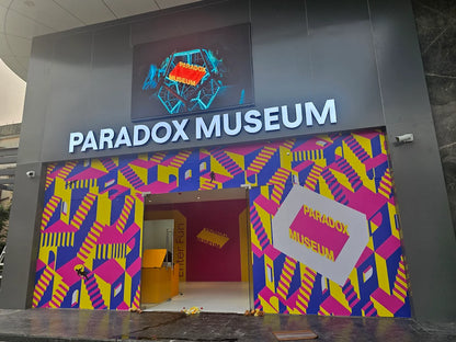 The Paradox Museum entrance features a vibrant, optical illusion mural of stairs and doorways, with the museum's name displayed prominently above.