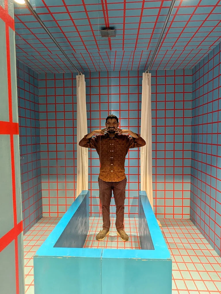 A man stands in a room with blue and red grid walls, posing in a blue bathtub.