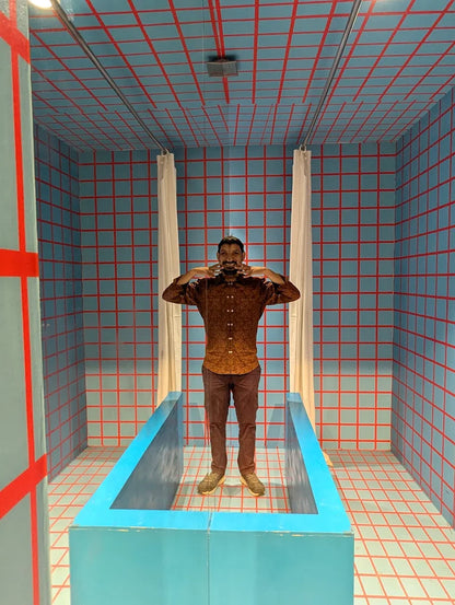 A man stands in a room with blue and red grid walls, posing in a blue bathtub.