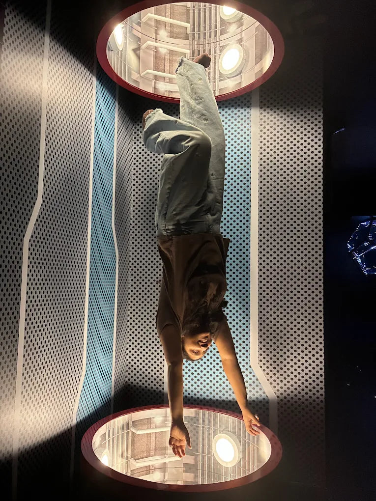 A person is upside down in a room with a perforated wall and circular light fixtures.