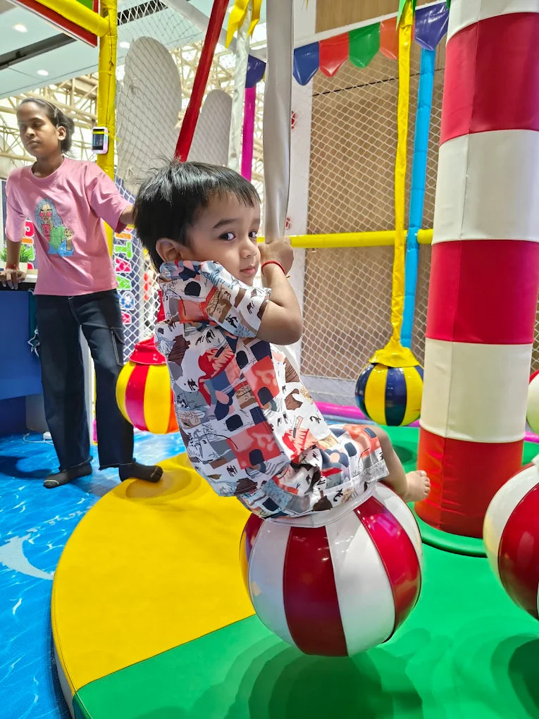 Child playing on a colorful playground structure with a striped pole and balls.