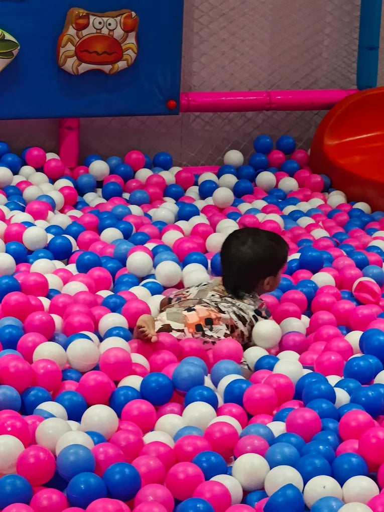 Child playing in a ball pit with pink, blue, and white balls.